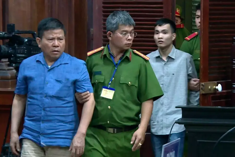 SATT I SAMME FENGSEL: Australske Chau Van Kham (til venstre) tas med til rettsalen i Ho Chi Minh-byen 11. november 2019. Da ble han dømt til tolv års fengsel – og slapp ikke ut før hele fire år senere.
         Foto: Nguyen Thanh Chung / AP / NTB